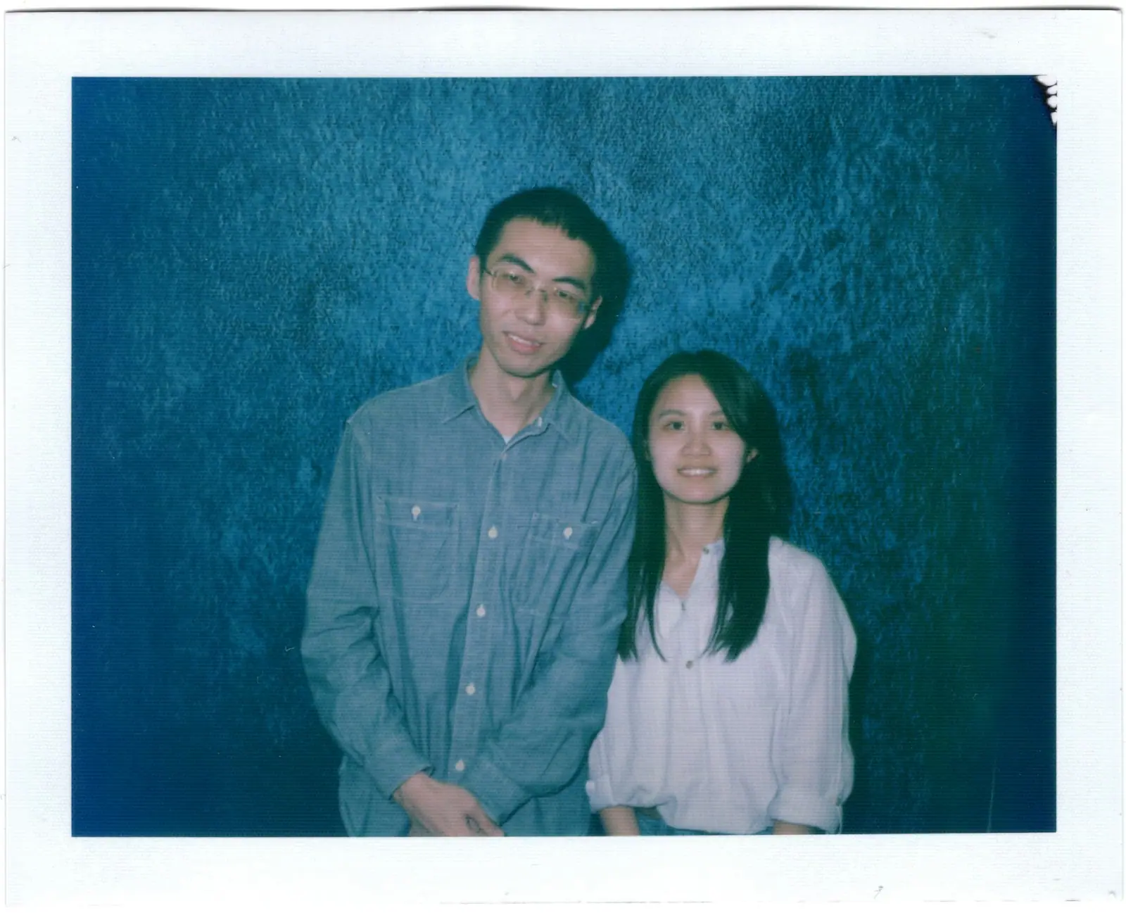 A young couple standing side by side against a blue wall