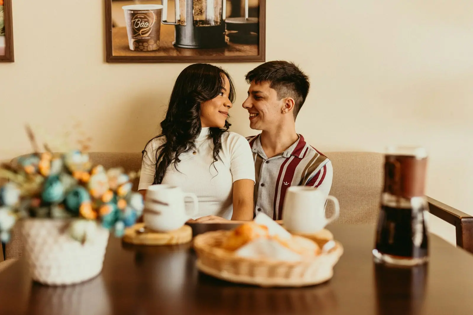 A couple sitting close at a café table, smiling at each other