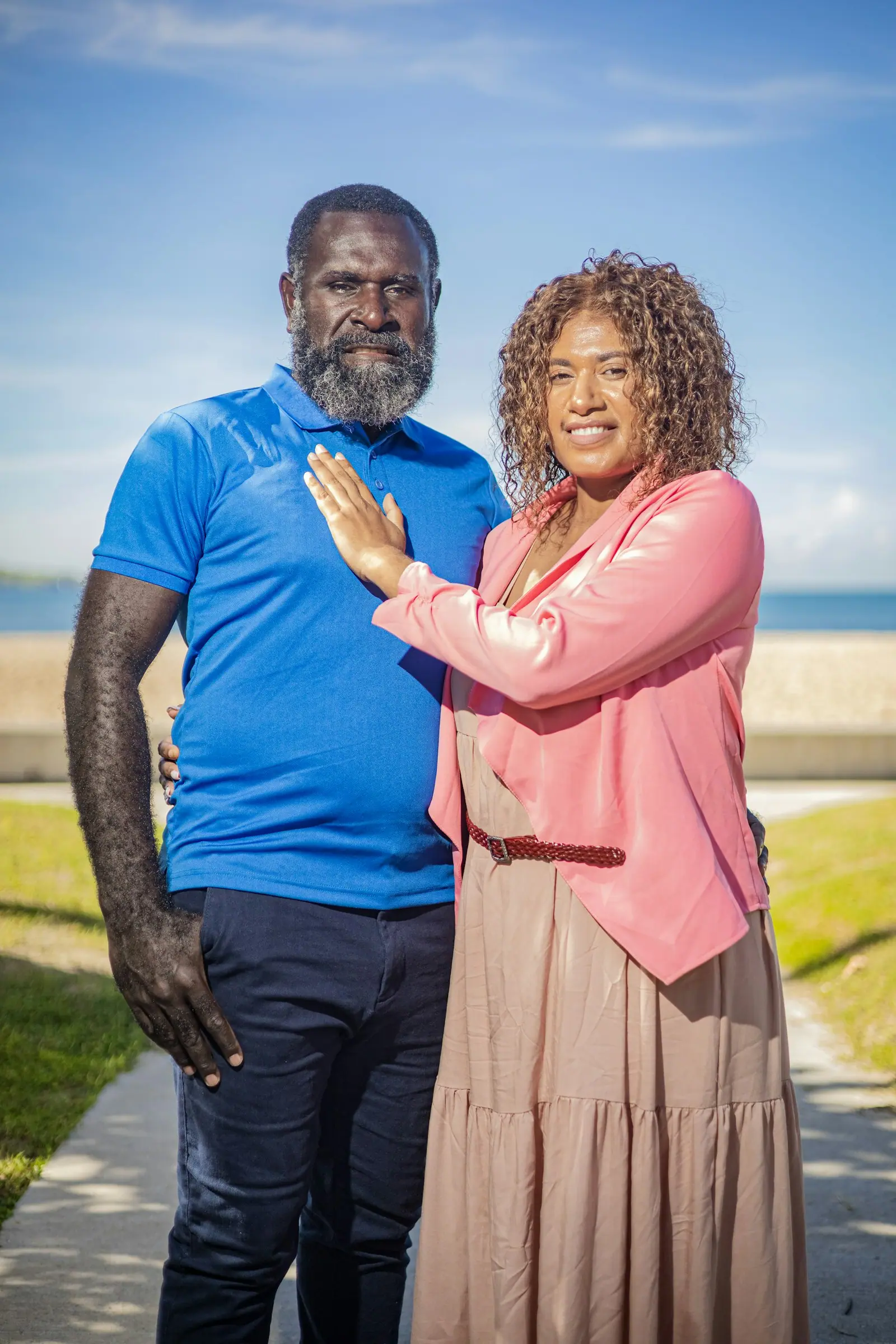 A husband and wife standing together outdoors, smiling