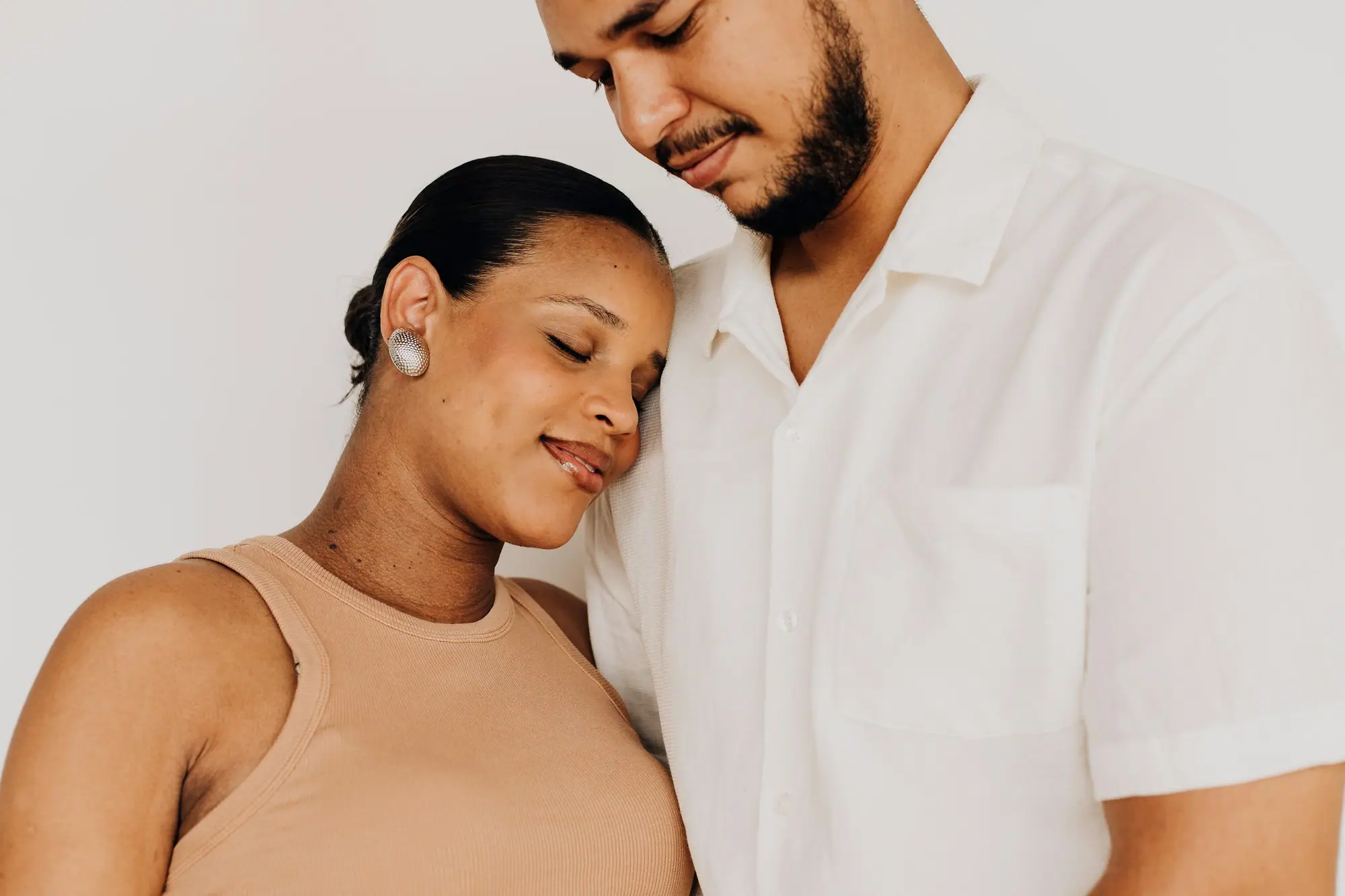 A husband holding his wife close, both smiling with their eyes closed