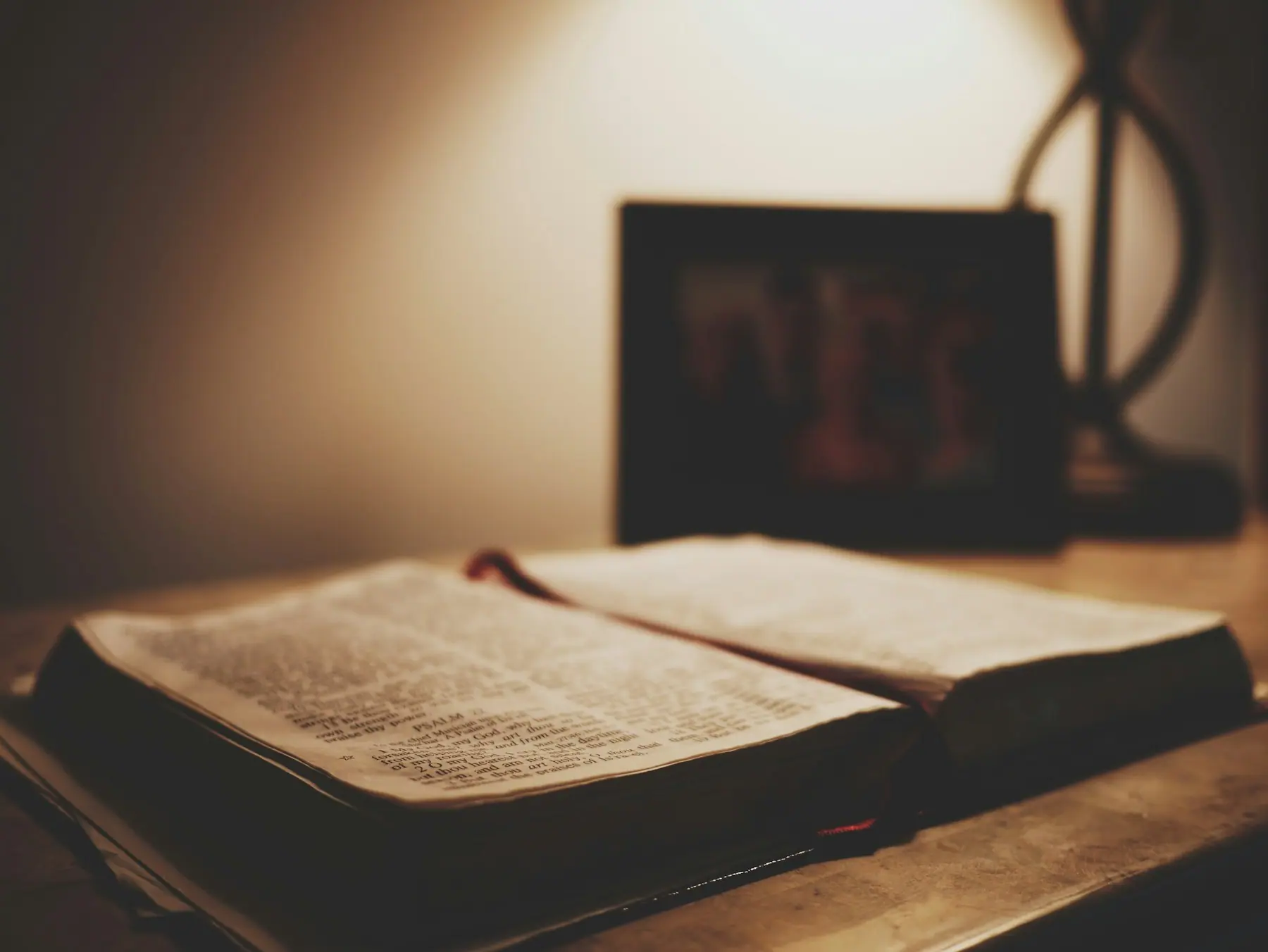 An open Bible on a desk under a warm lamp
